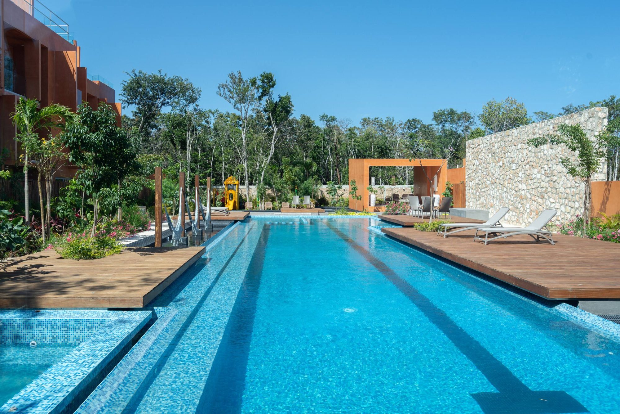 Long lap-style community pool lined with wooden decks, loungers and palms